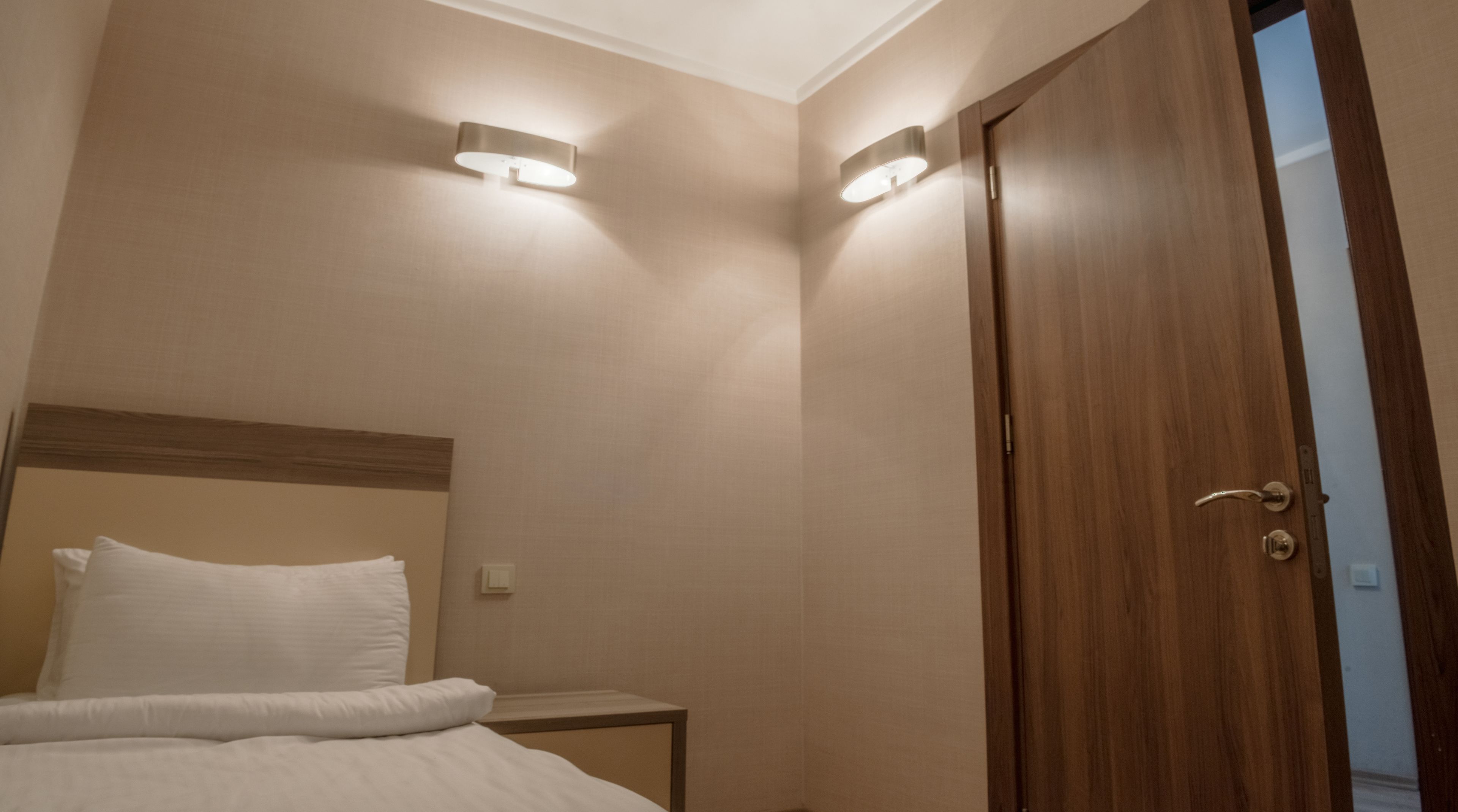 A hotel room with a bed, a nightstand, and a wooden door.