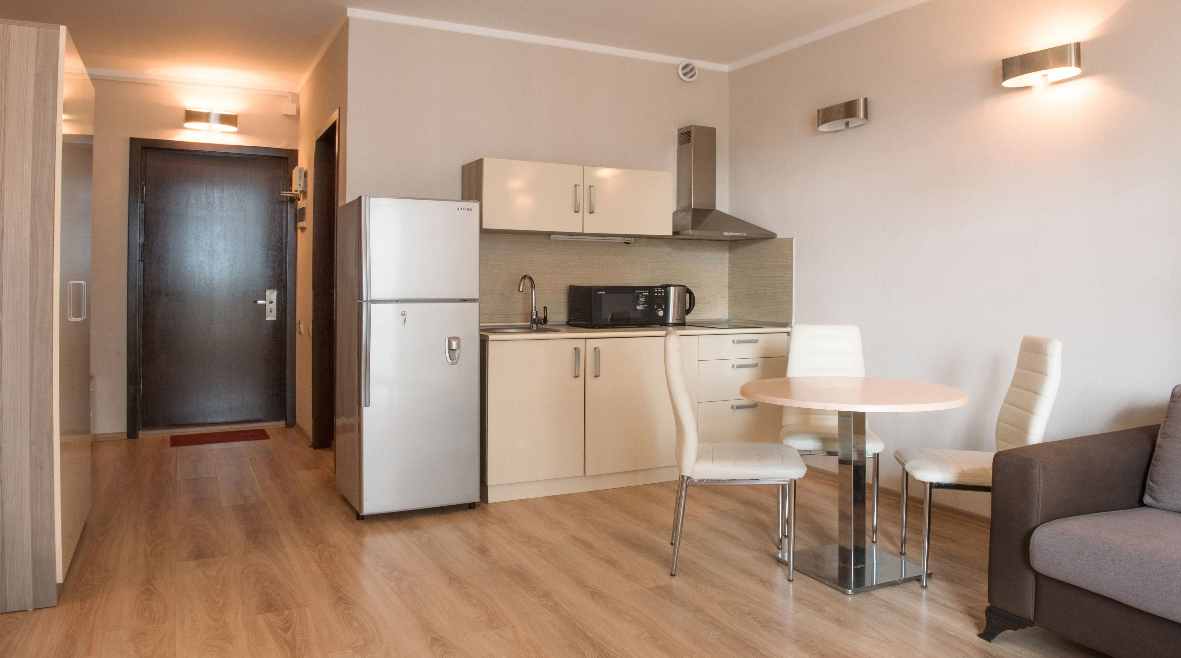 A compact kitchen with a refrigerator, microwave, and stove, a dining table with chairs, and a sofa.