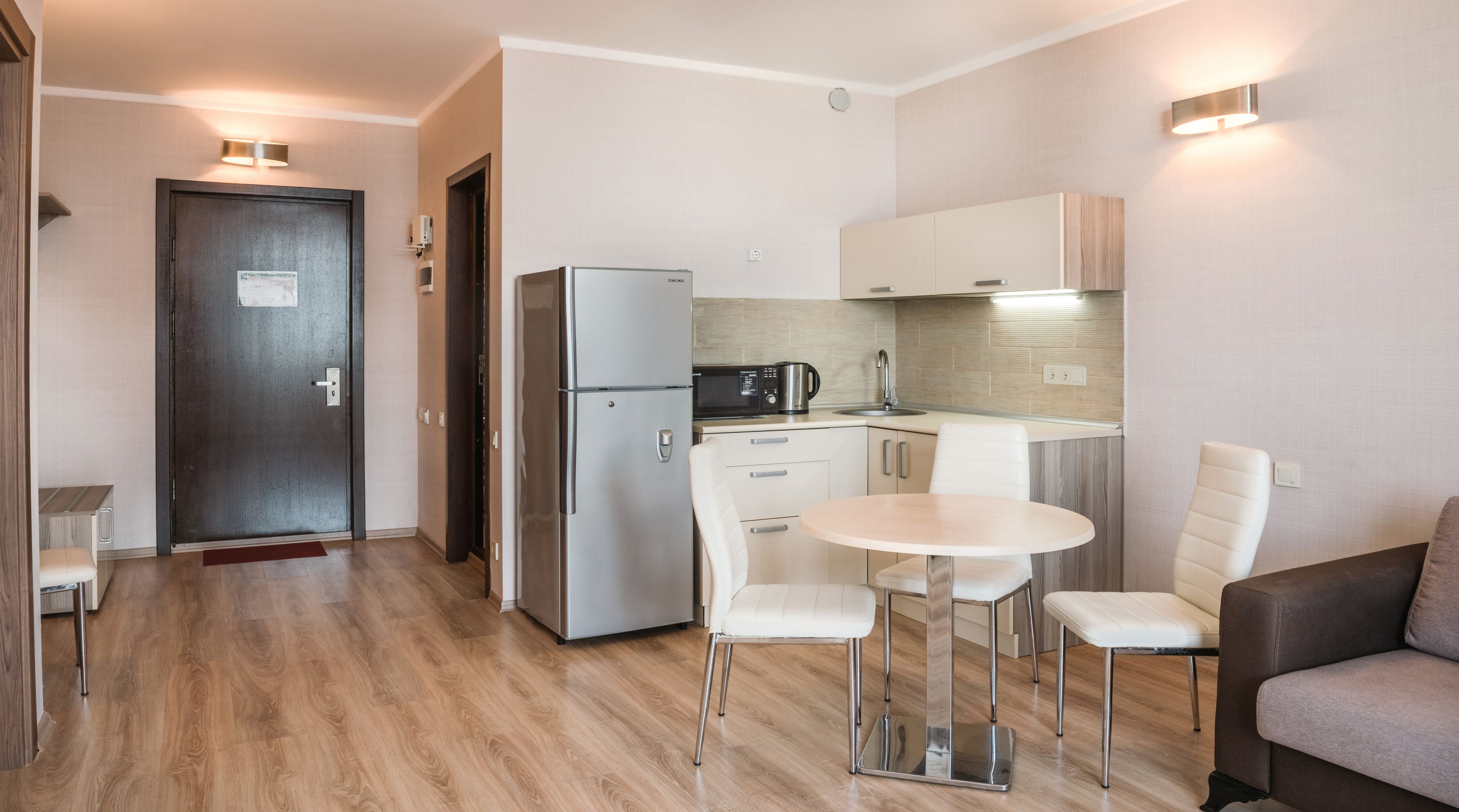 Een compacte keuken met een koelkast, magnetron en een klein zitehoekje met twee stoelen en een tafel.