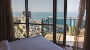 A hotel room with a large window offering a view of the beach and cityscape. - Silk Road Sea Towers Batumi Apart Hotel (Batumi)