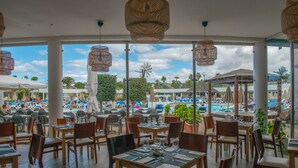 An outdoor dining area with tables and chairs, large windows overlooking a pool and resort area. - Relaxia Lanzasur- All Inclusive (Yaiza)