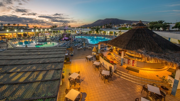 A resort pool area with lounge chairs and umbrellas, a bar, and a view of a mountain. - Relaxia Lanzasur- All Inclusive (Yaiza)