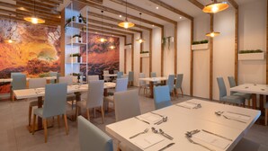 A modern dining area with white tables, blue chairs, and pendant lighting. - Relaxia Lanzasur- All Inclusive (Yaiza)