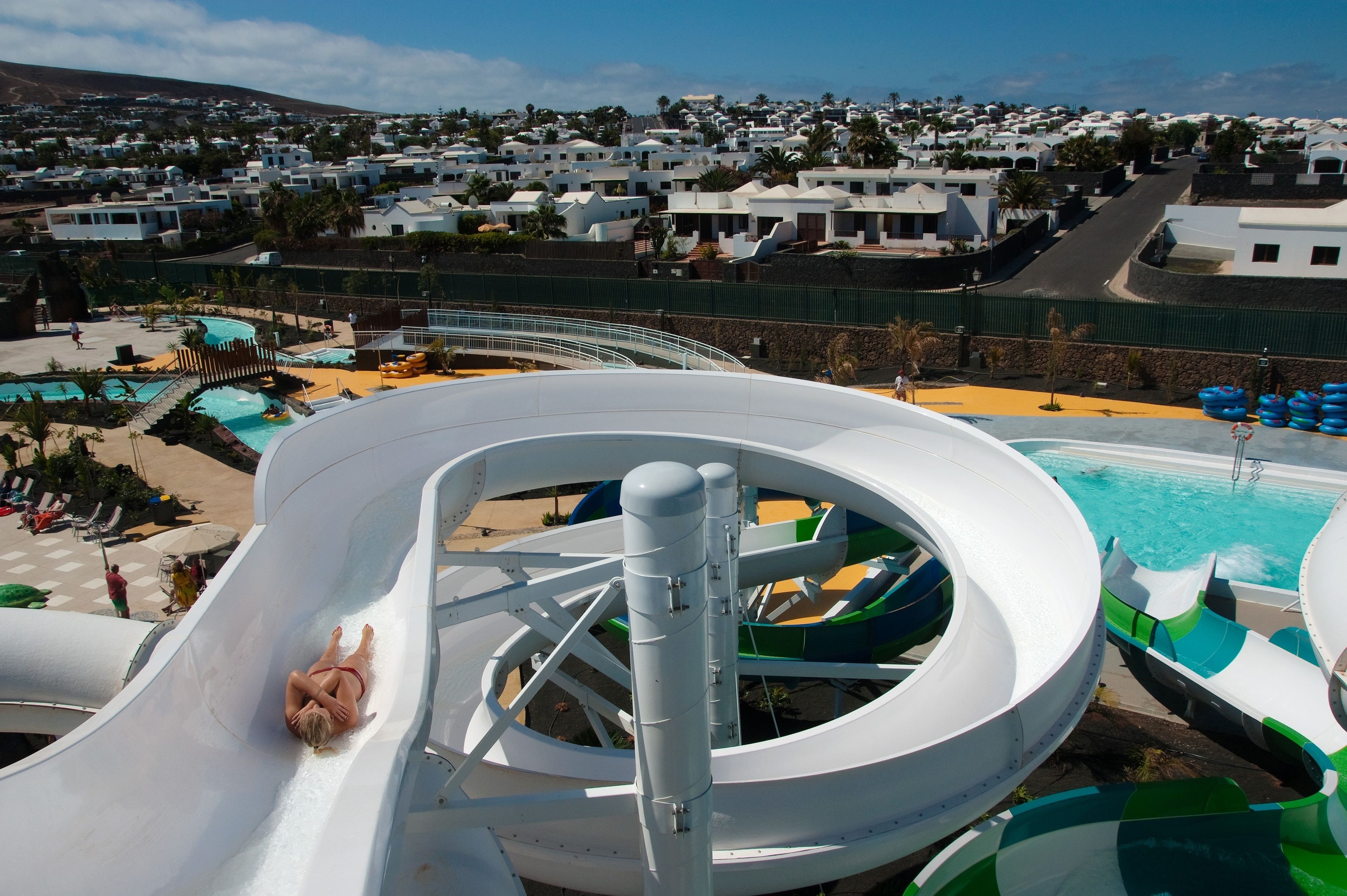 Un toboggan aquatique dans un complexe hôtelier doté d’une piscine et offrant une vue sur un village côtier.