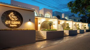 Exterior de un hotel con un letrero de neón circular que dice "DE LUNA Laputa", múltiples ventanas arqueadas y un paseo empedrado.