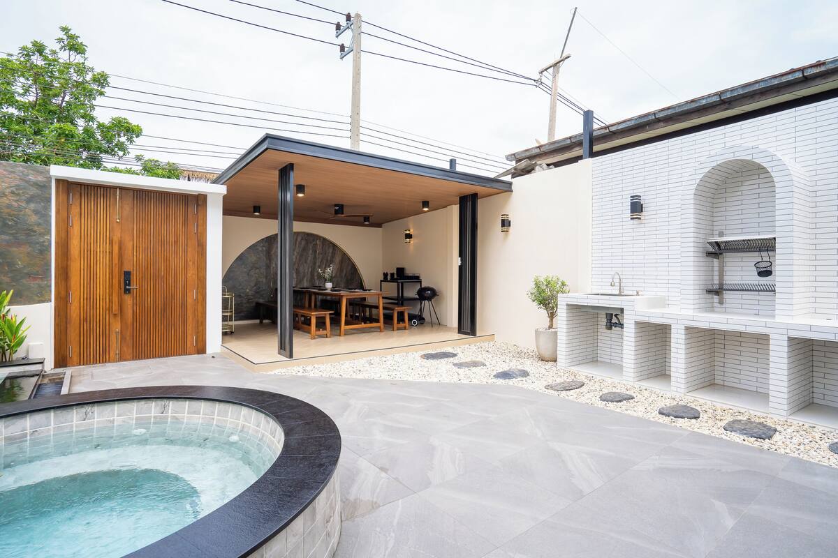 A modern outdoor patio with a hot tub, a wooden deck, and a barbecue area.