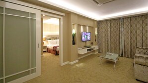A hotel room with a bed, a TV, a glass coffee table, a sofa, and a sliding door leading to another room. - The Guest Hotel & Spa (Port Dickson)