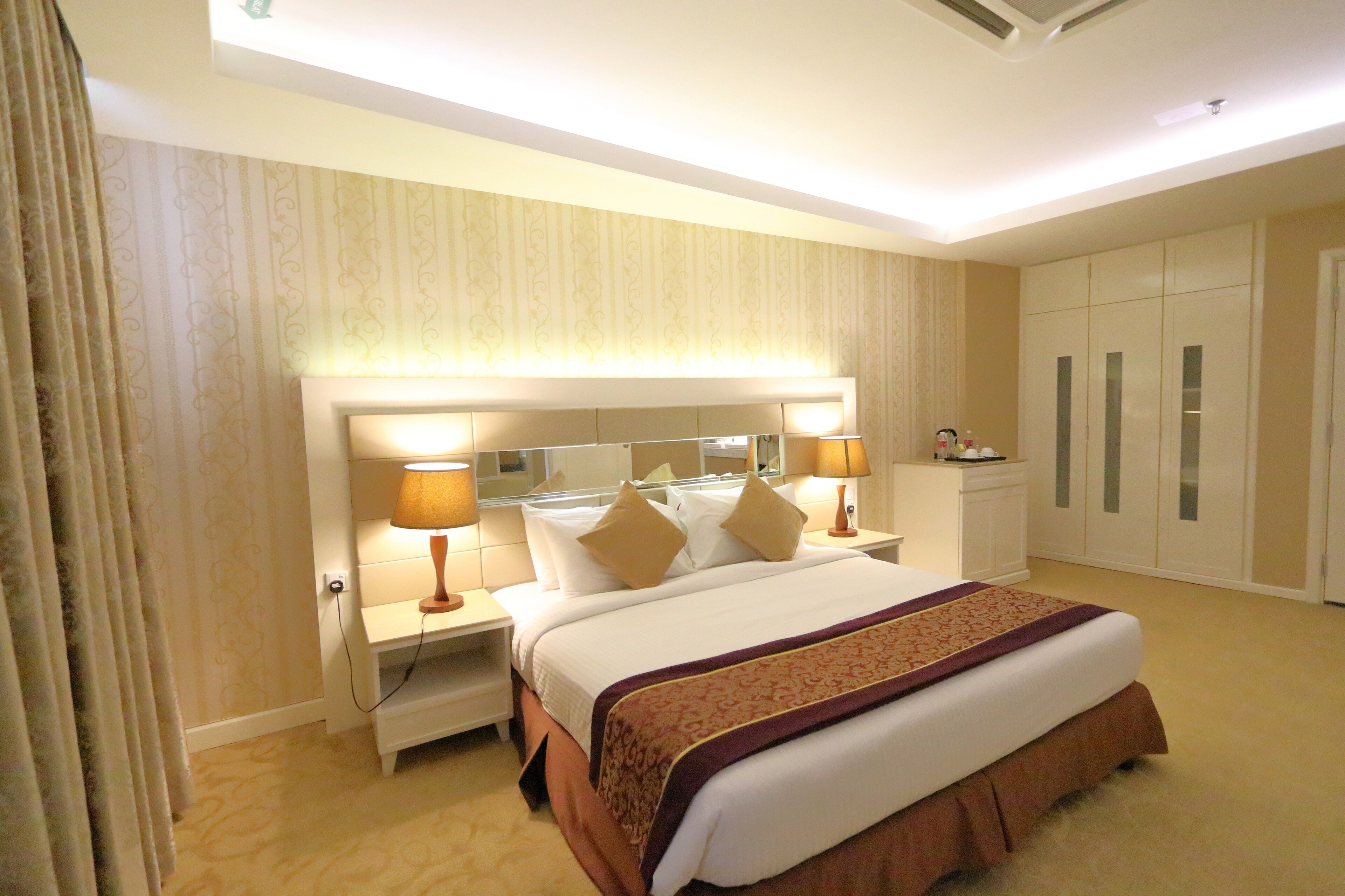 A hotel room with a large bed, two bedside tables with lamps, a wardrobe, and a mirror above the bed.