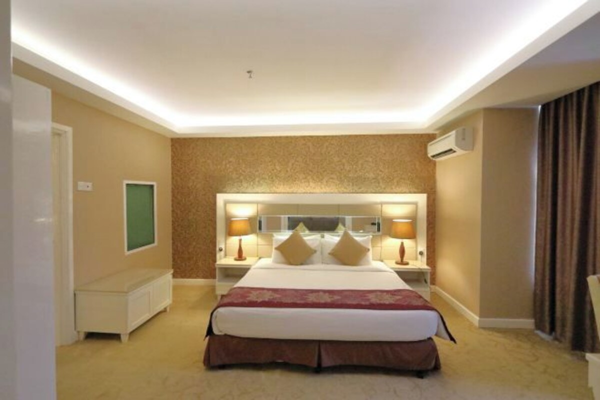 Une chambre d’hôtel avec un grand lit, des lampes de chevet, une tête de lit agrémentée d’un miroir et un appareil de climatisation.