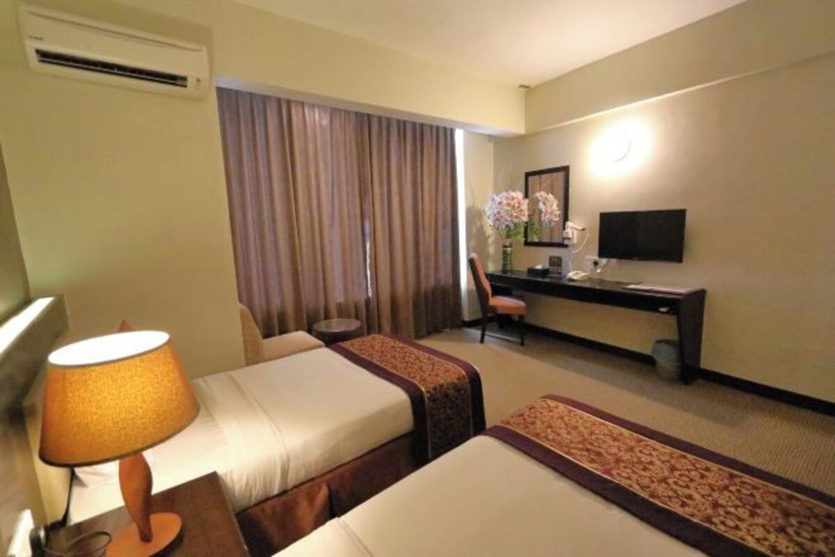 A hotel room with two beds, a desk with a chair, a TV, and an air conditioning unit.