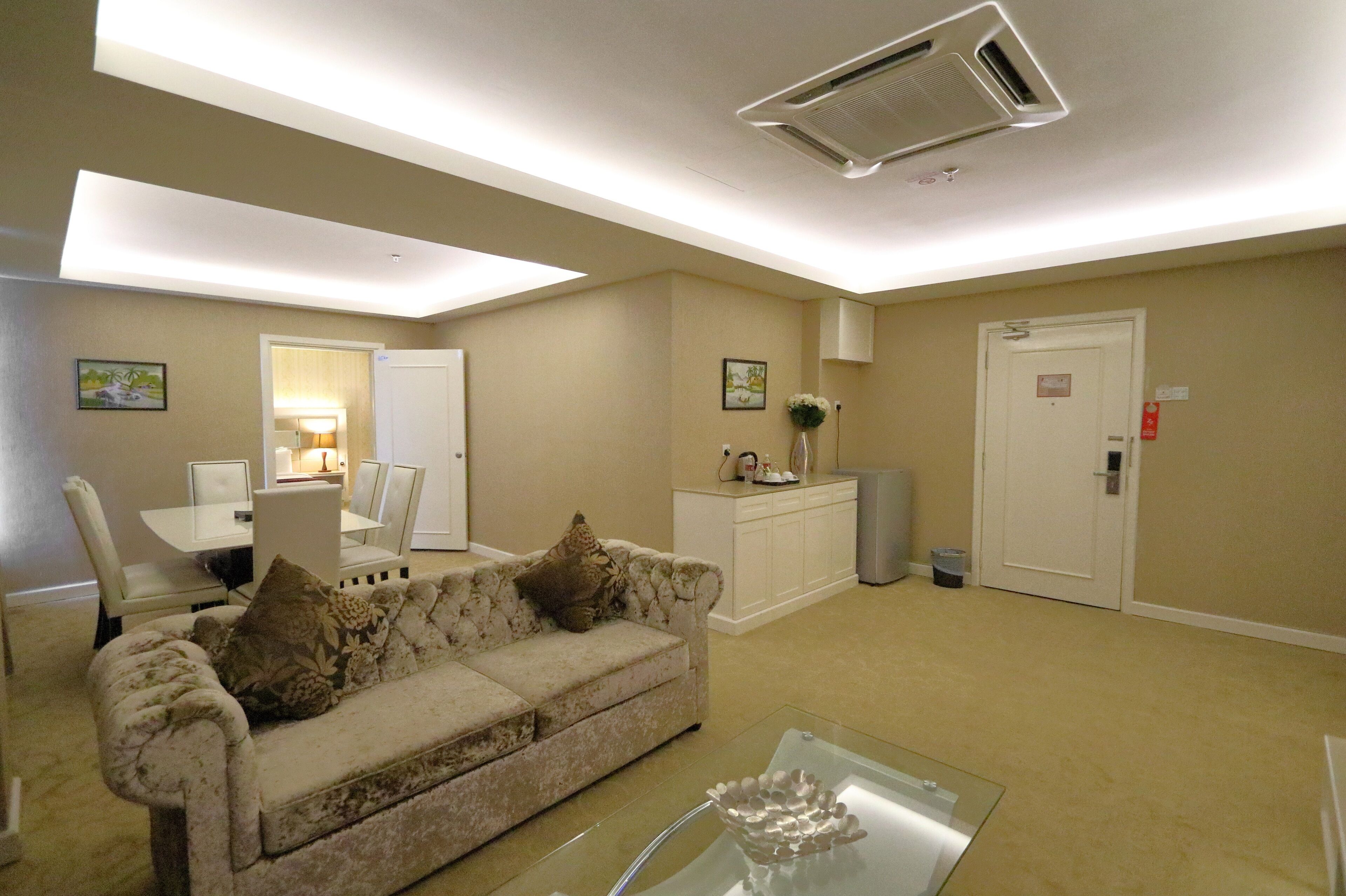 A living room with a beige sofa, a glass coffee table, a white cabinet, and a dining area with a table and chairs.