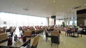 A spacious restaurant with multiple dining tables and chairs, large windows, and ceiling lights.