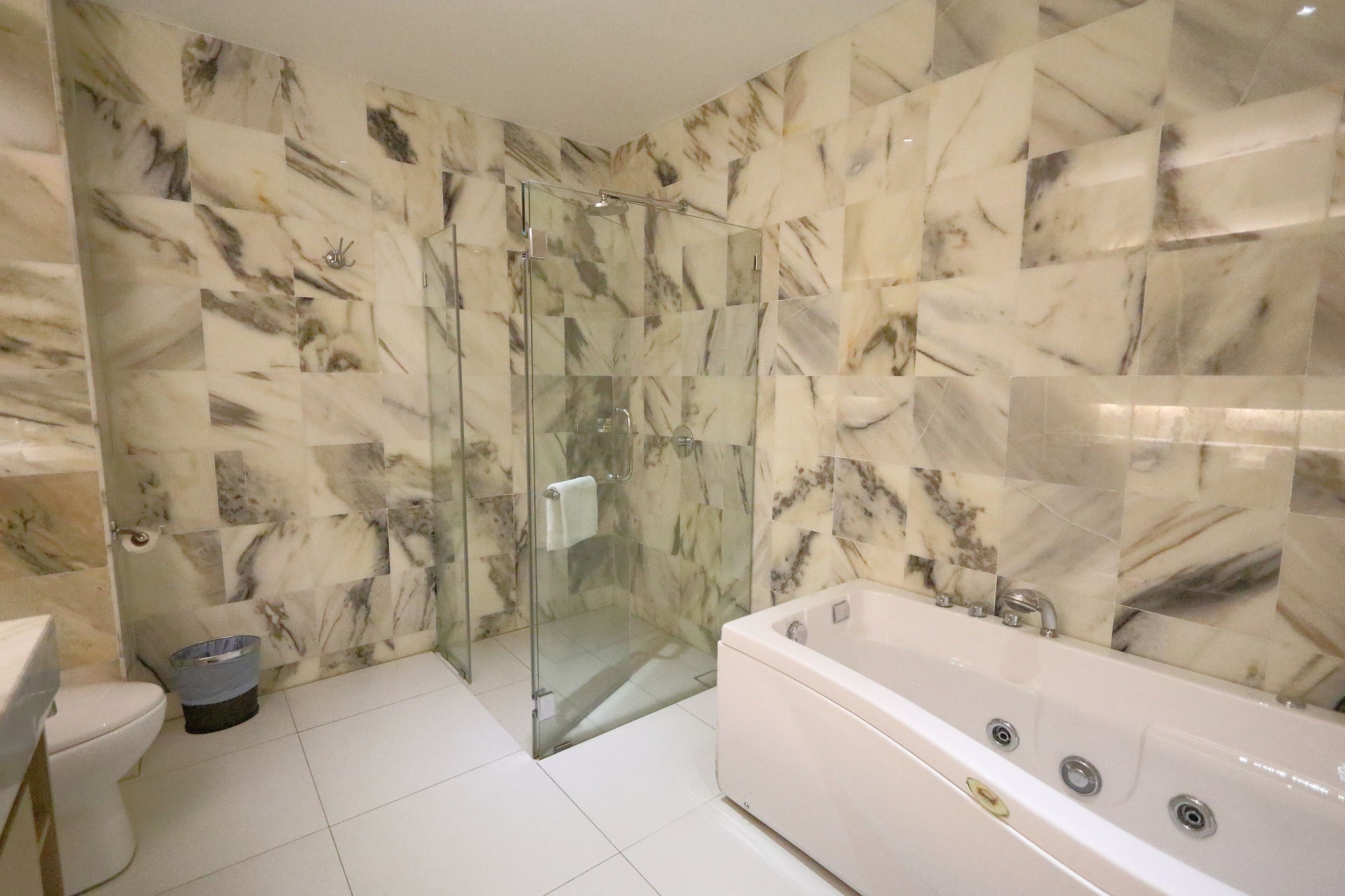 A modern bathroom with a glass-enclosed shower, a white bathtub, and marble-patterned walls.
