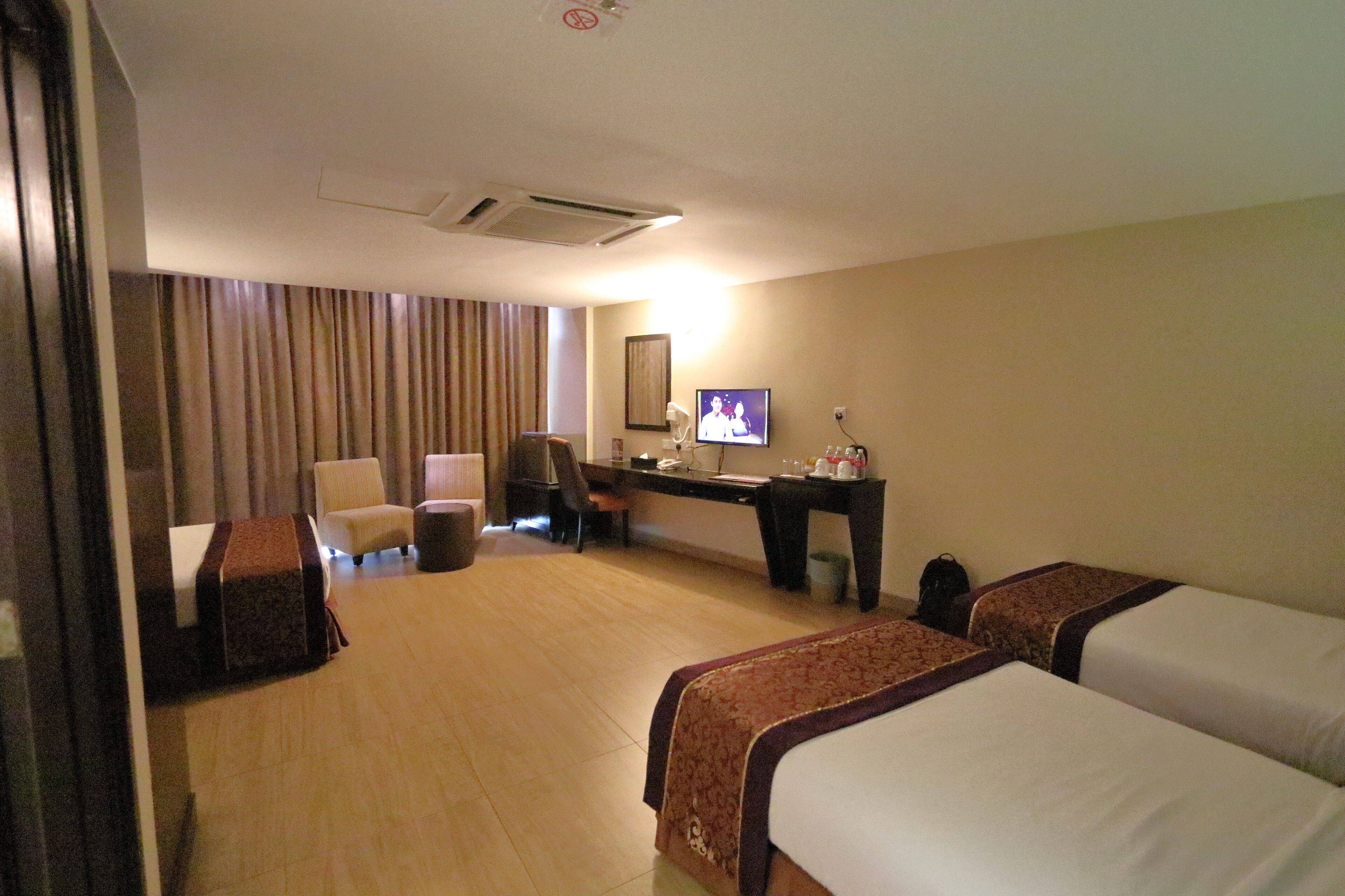 A hotel room with two beds, a desk, a chair, a television, and a large window with curtains.