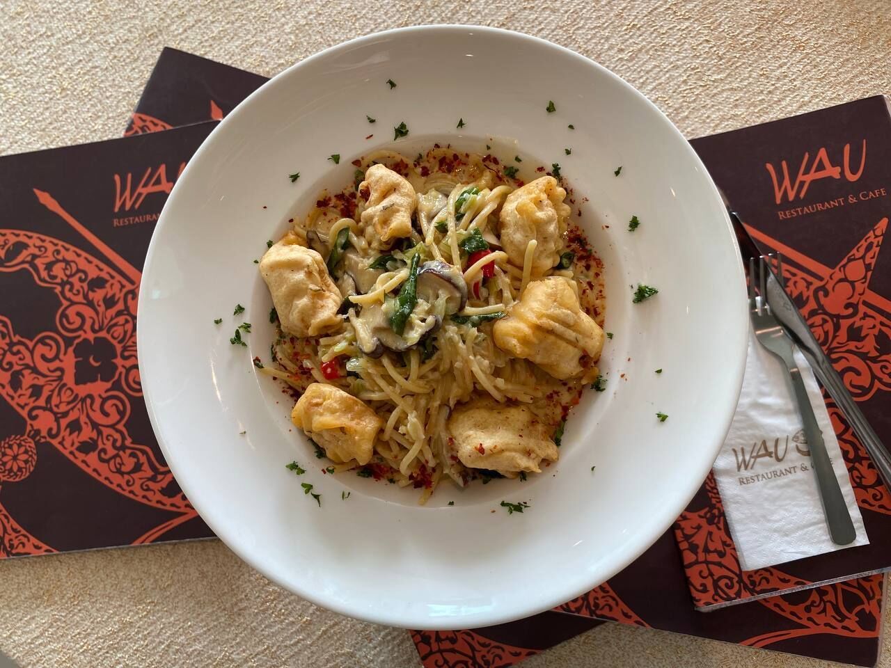 Un plat de pâtes au poulet et aux légumes, posé sur une table avec une serviette et un menu.