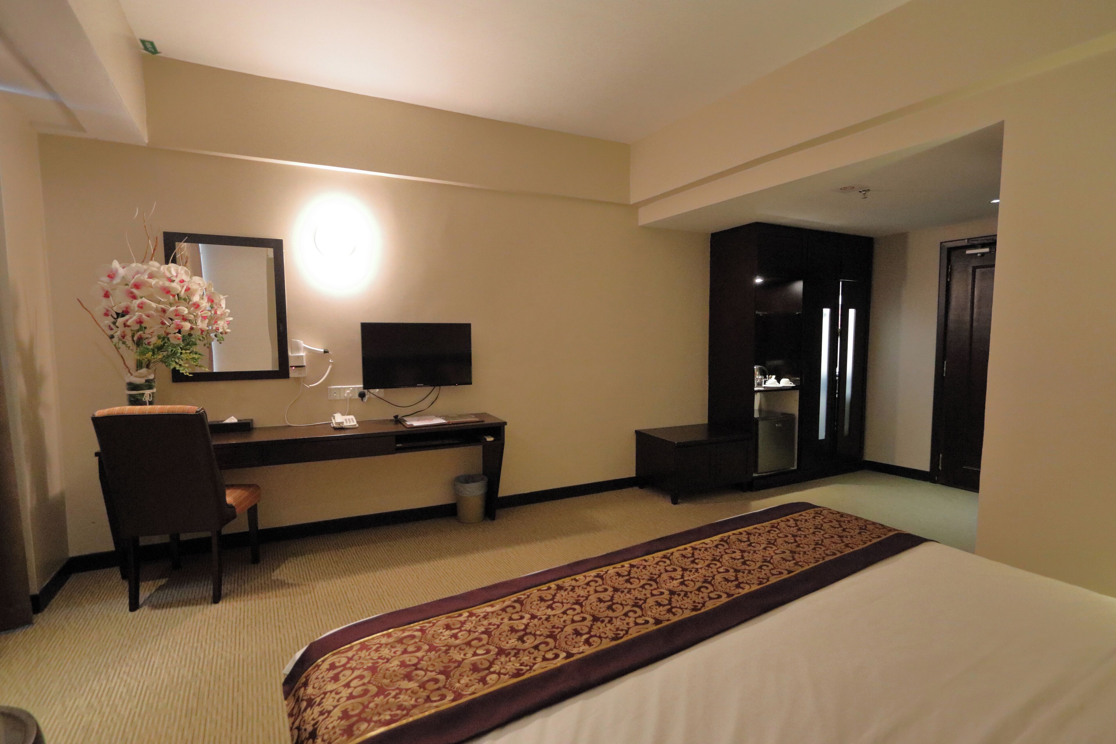 Habitación de hotel con cama, escritorio con silla, espejo, televisión y baño visible a través de una puerta abierta.