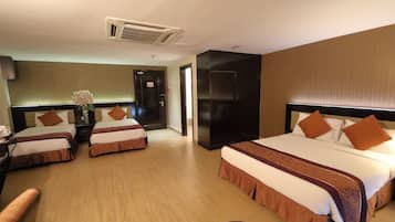 A hotel room with three beds, a desk, a chair, and a small table with a vase of flowers.