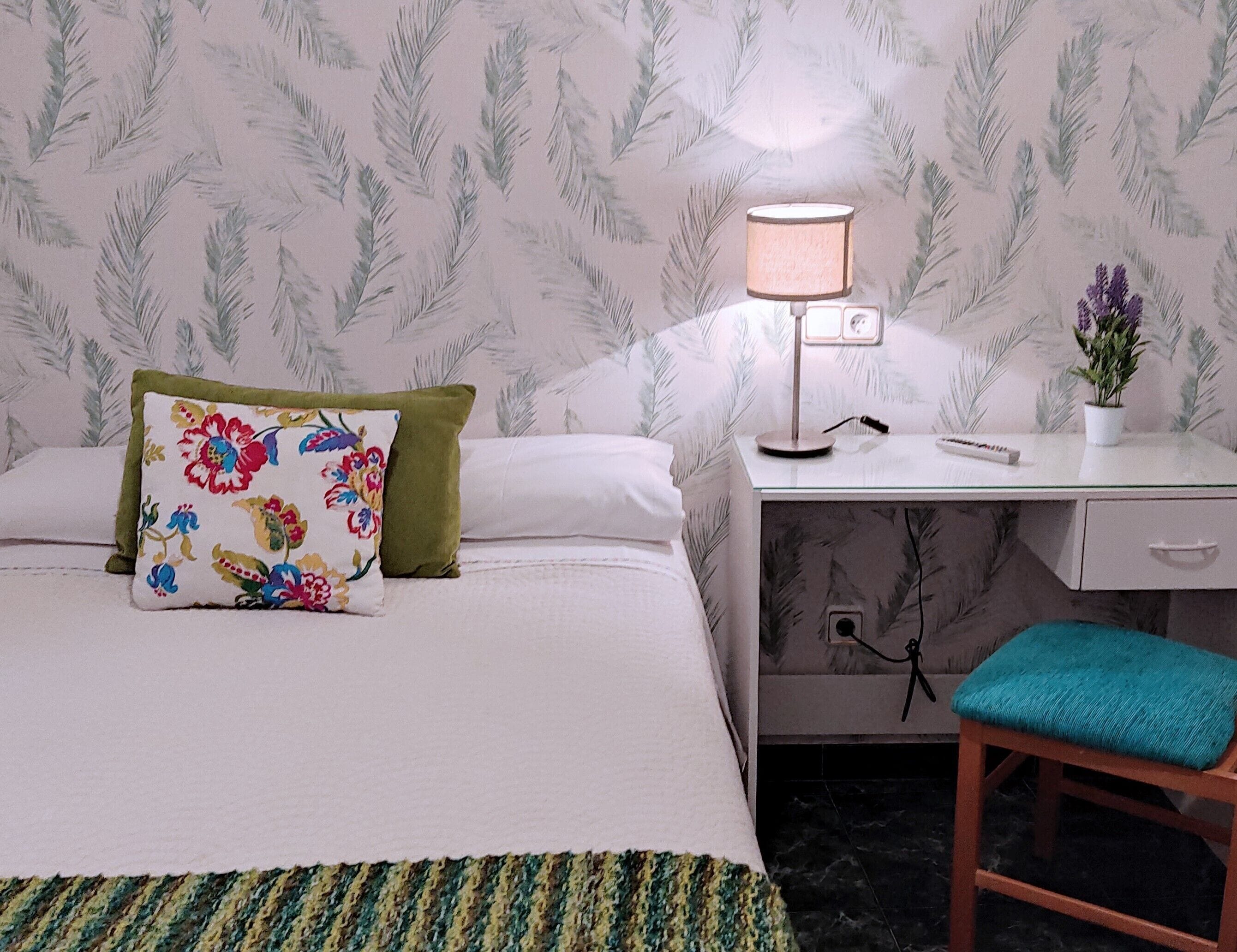 A hotel room with a bed, a desk, a chair, and a lamp.
