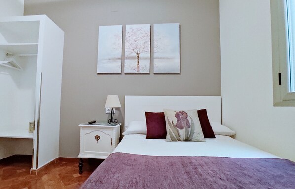 A bedroom with a bed, nightstand, and a wardrobe. There are three wall-mounted paintings above the bed.