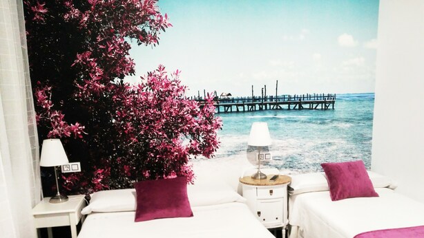 A hotel room with two beds, a nightstand with a lamp, and a view of a pier over water. - Hostal Bruña (Madrid)