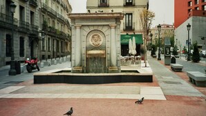 A public square with a fountain, benches, and a building with a green awning. - Hostal Bruña (Madrid)
