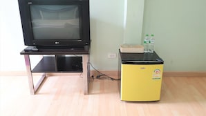 A television on a stand with a remote control, a small yellow appliance, and a water bottle on a table. - Sea Beach Koh Larn 2 (Koh Lan)