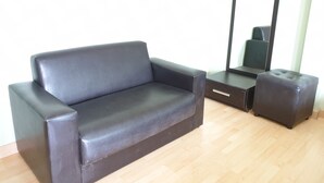 A dark-colored sofa and ottoman in a room with wooden flooring and a large mirror on the wall. - Sea Beach Koh Larn 2 (Koh Lan)