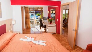 A hotel room with a bed, a desk, and a view of a pool area. - Aegean View Aqua Resort (Kos)
