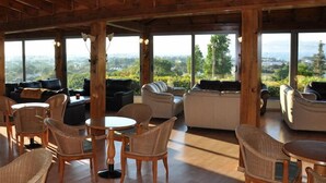 A spacious indoor area with wicker furniture, large windows, and a view of the landscape. - Aegean View Aqua Resort (Kos)