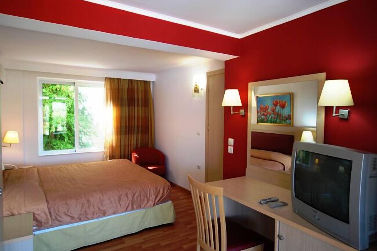 A hotel room with a bed, a desk with a TV, and a window with curtains.