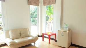 A room with a beige sofa, a small red table, and a white refrigerator. - Sea Beach Koh Larn 3 (Koh Lan)