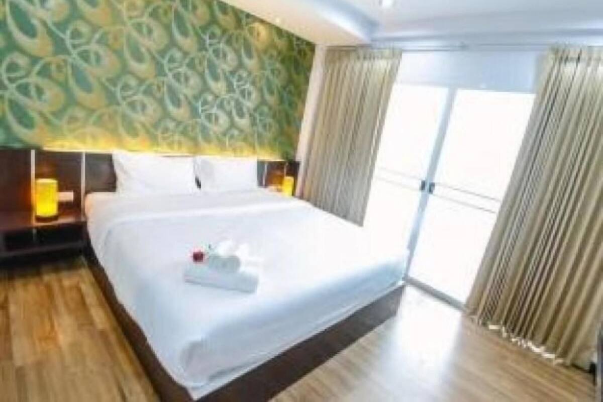 Ein Hotelzimmer mit einem großen Bett, einem Nachttisch, einer Lampe und Blick ins Freie.
