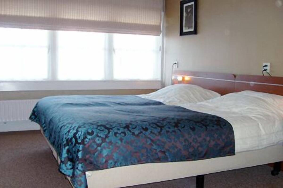 Cama com colcha estampada, travesseiro branco e cabeceira com interruptor de luz.