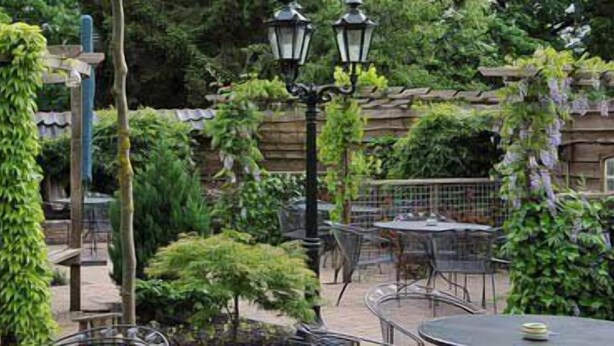Een terras buiten met houten pergola’s, tafels en stoelen.
