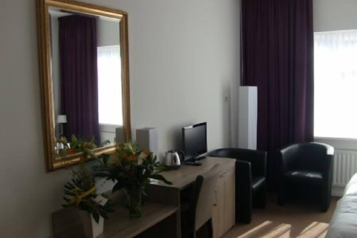 Quarto de hotel com escrivaninha, cadeira, televisão e cama.