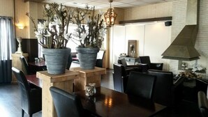 Een restaurantinterieur met houten tafels en stoelen, grote potplanten en een hangende lamp.
