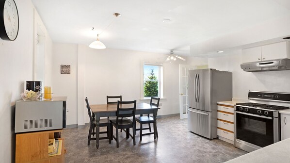 A modern kitchen with a dining table, chairs, a refrigerator, stove, and a ceiling fan.