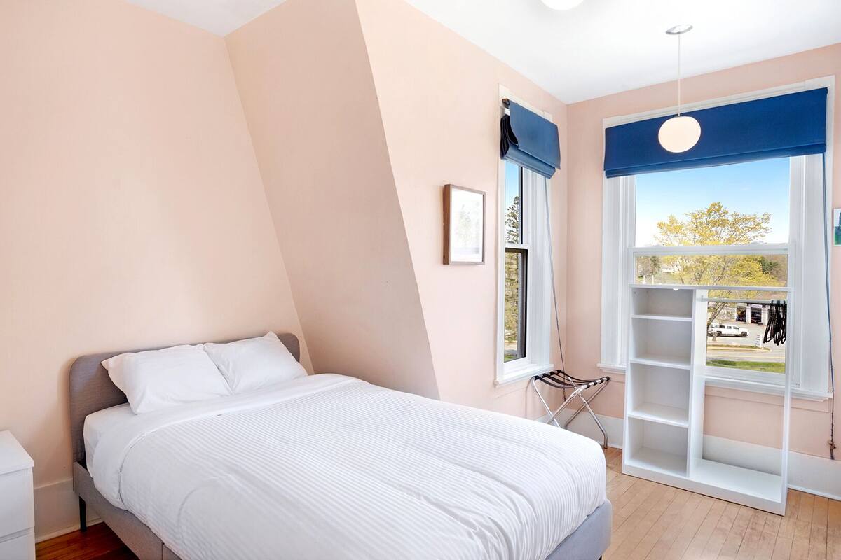 A bedroom with a bed, a bedside table, a window with a view, and a built-in shelf.