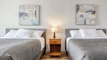 A hotel room with two beds, a nightstand with a lamp, and abstract wall art.