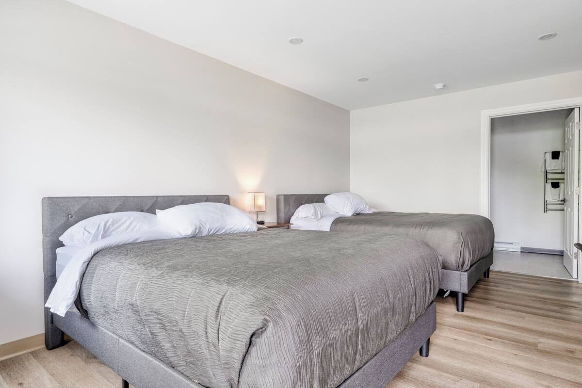 A modern hotel room with two beds, a wooden floor, and a white wall.