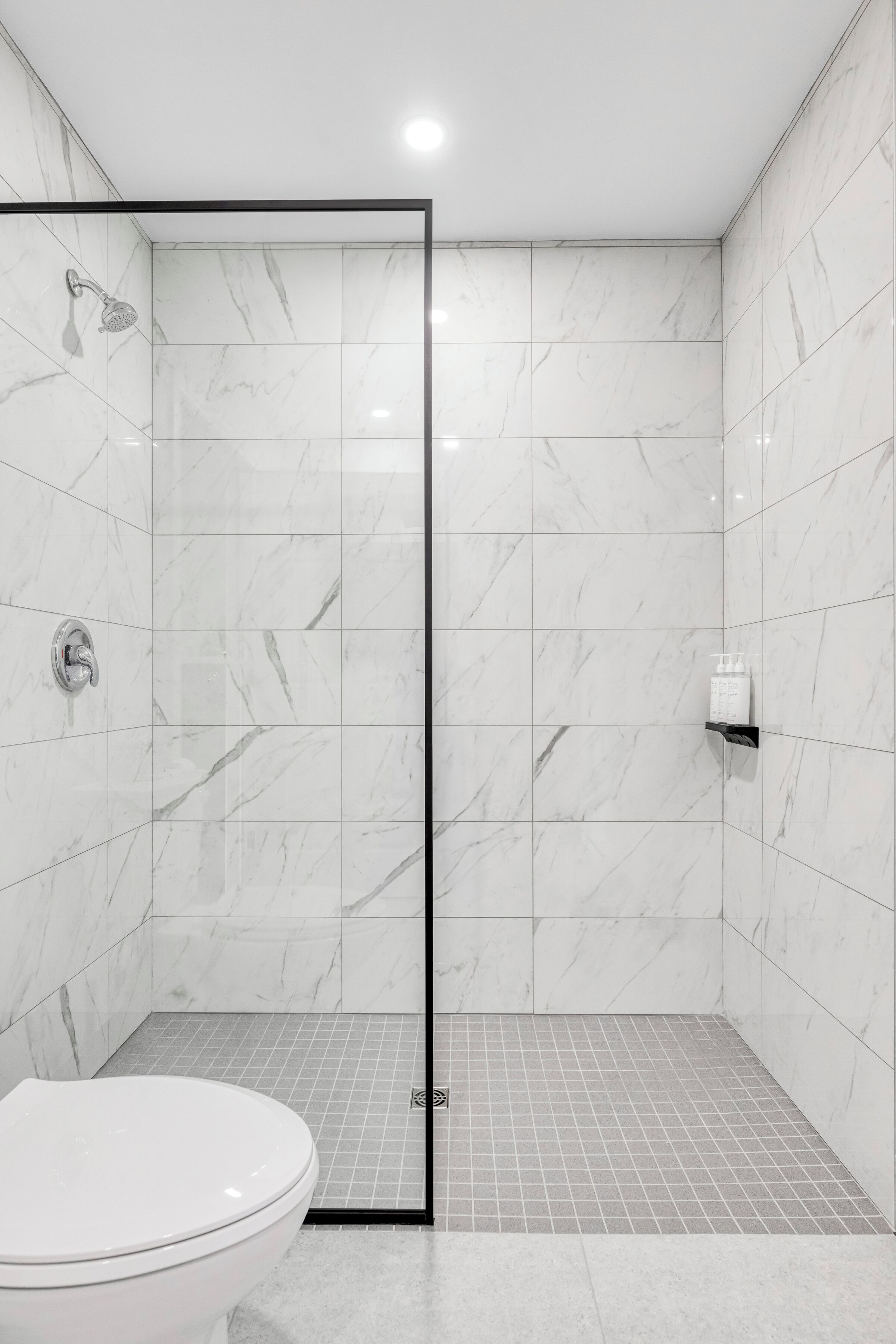 A modern bathroom with a shower, toilet, and tiled floor.