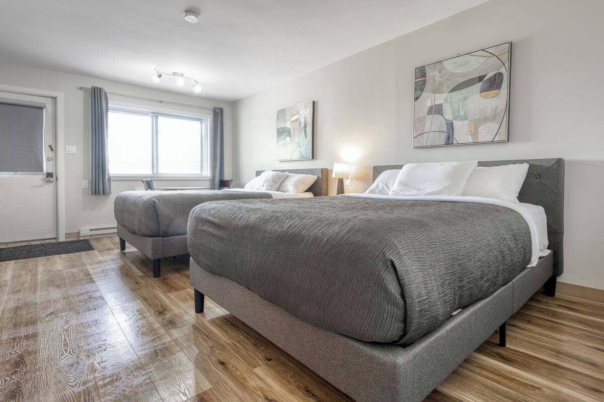 A hotel room with two beds, a large window, and artwork on the walls.