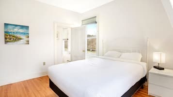 Un dormitorio con una cama grande, una mesita de noche con lámpara, una ventana con persianas y un cuadro en la pared.