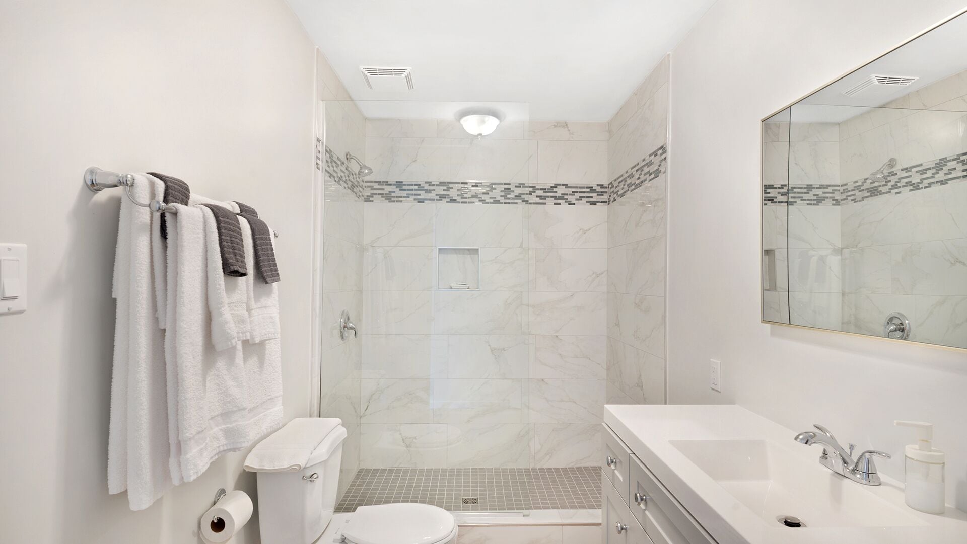 Un baño moderno con ducha envuelta en vidrio, inodoro, lavamanos y un espejo grande.