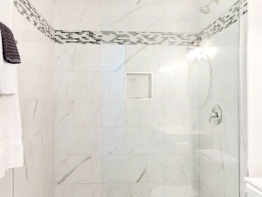 A shower with a glass door, a white toilet, and a wooden floor.