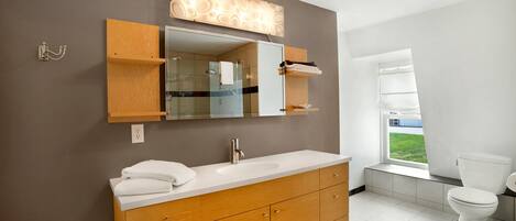 A modern bathroom with a wooden vanity, a large mirror, and a view of the outdoors through a window.