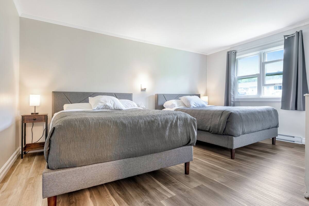A hotel room with two beds, wooden flooring, and a window with curtains.