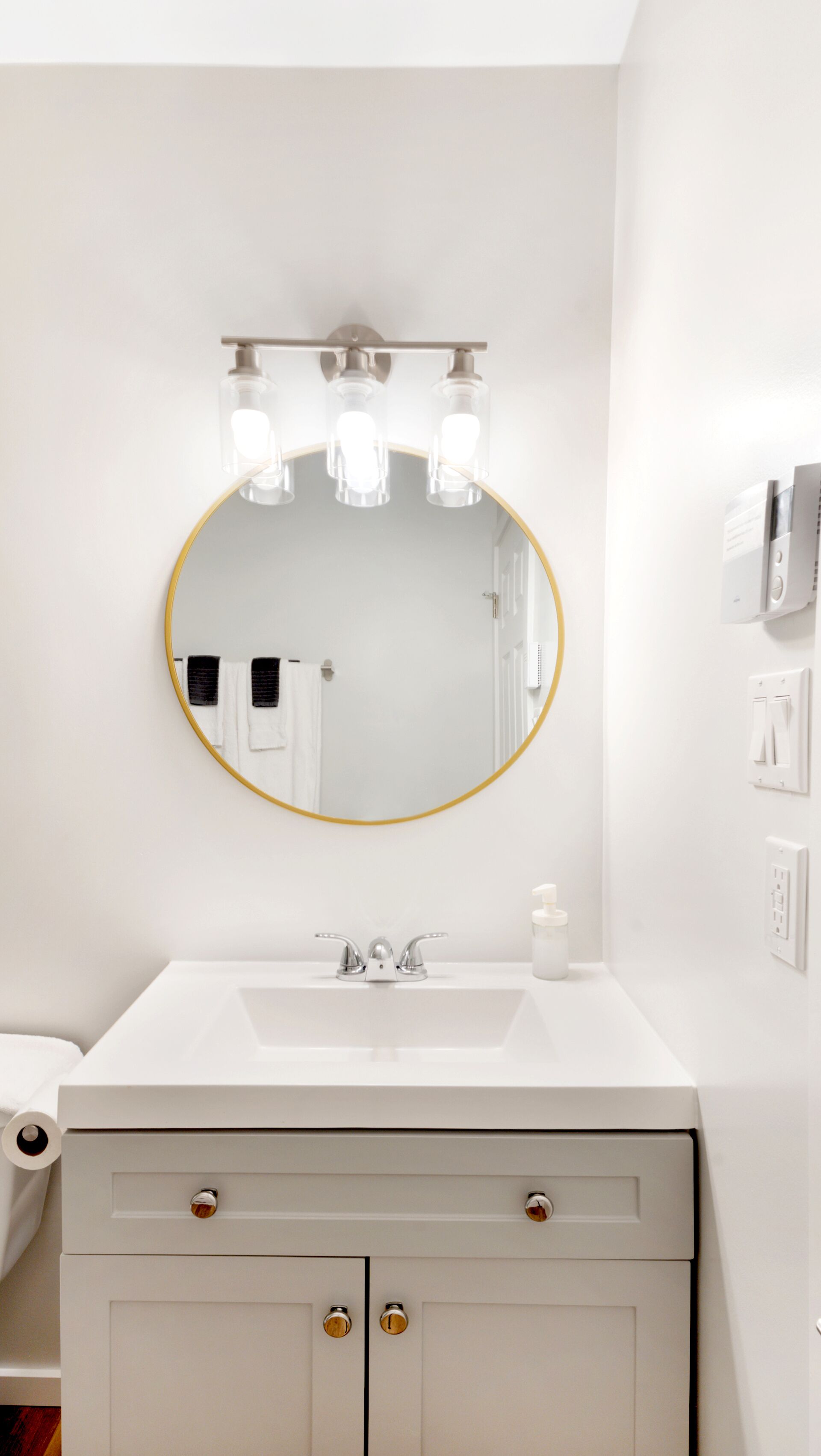Een badkamer met een ronde spiegel, een witte wasbak en een handdoekrek.
