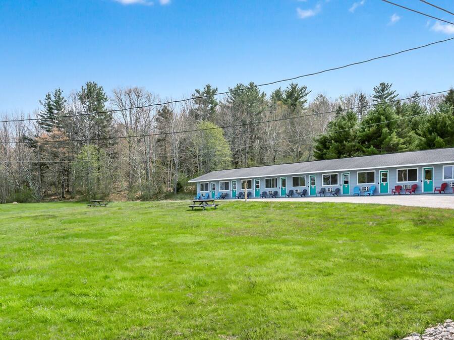 A motel with a row of rooms, each with a door and windows. There is a picnic table in the front yard.