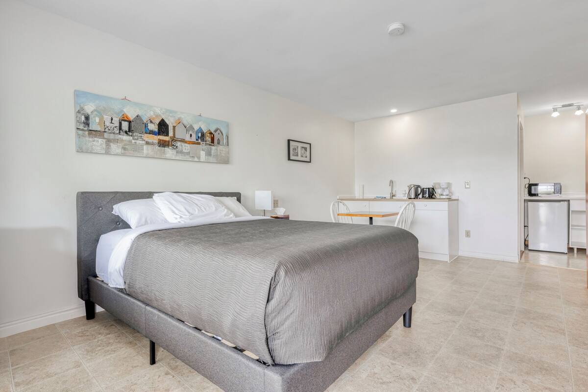 A modern bedroom with a large bed, a desk, and a kitchenette.